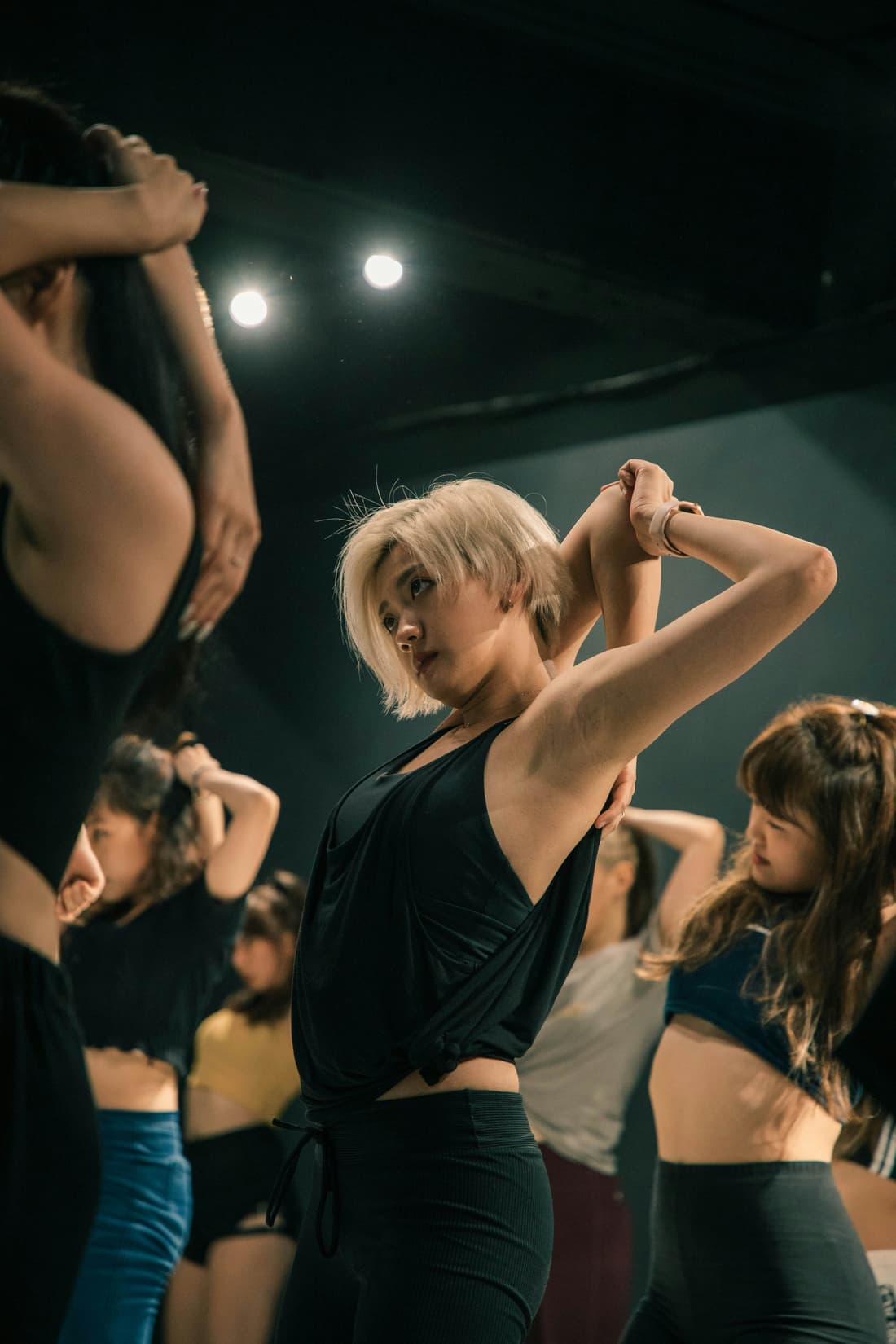 Une professeure mène un cours de danse, ses élèves reprennent le mouvement derrière elle.